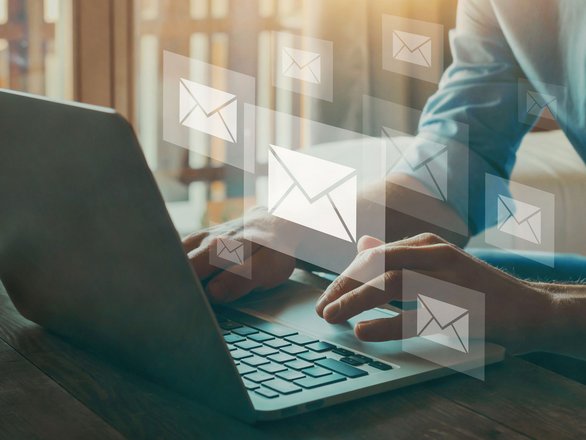 Person am Laptop mit schwebenden Briefsymbolen als Hinweis auf E-Mail-Newsletter.